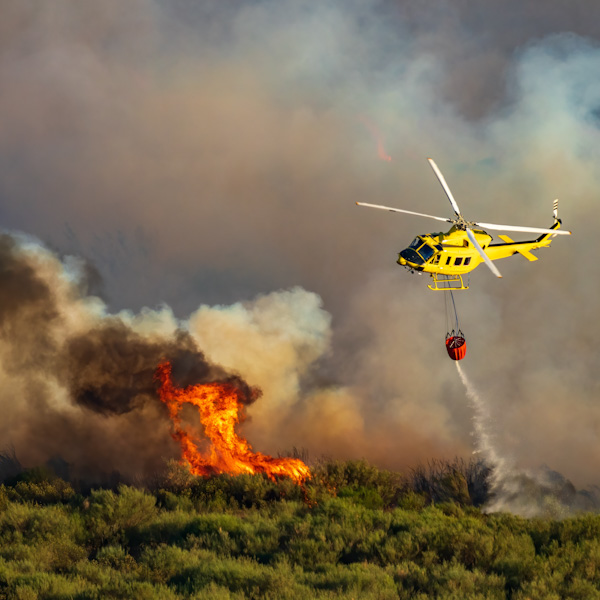 Helicopter with a bambi bucket dumping water over wildfire flames