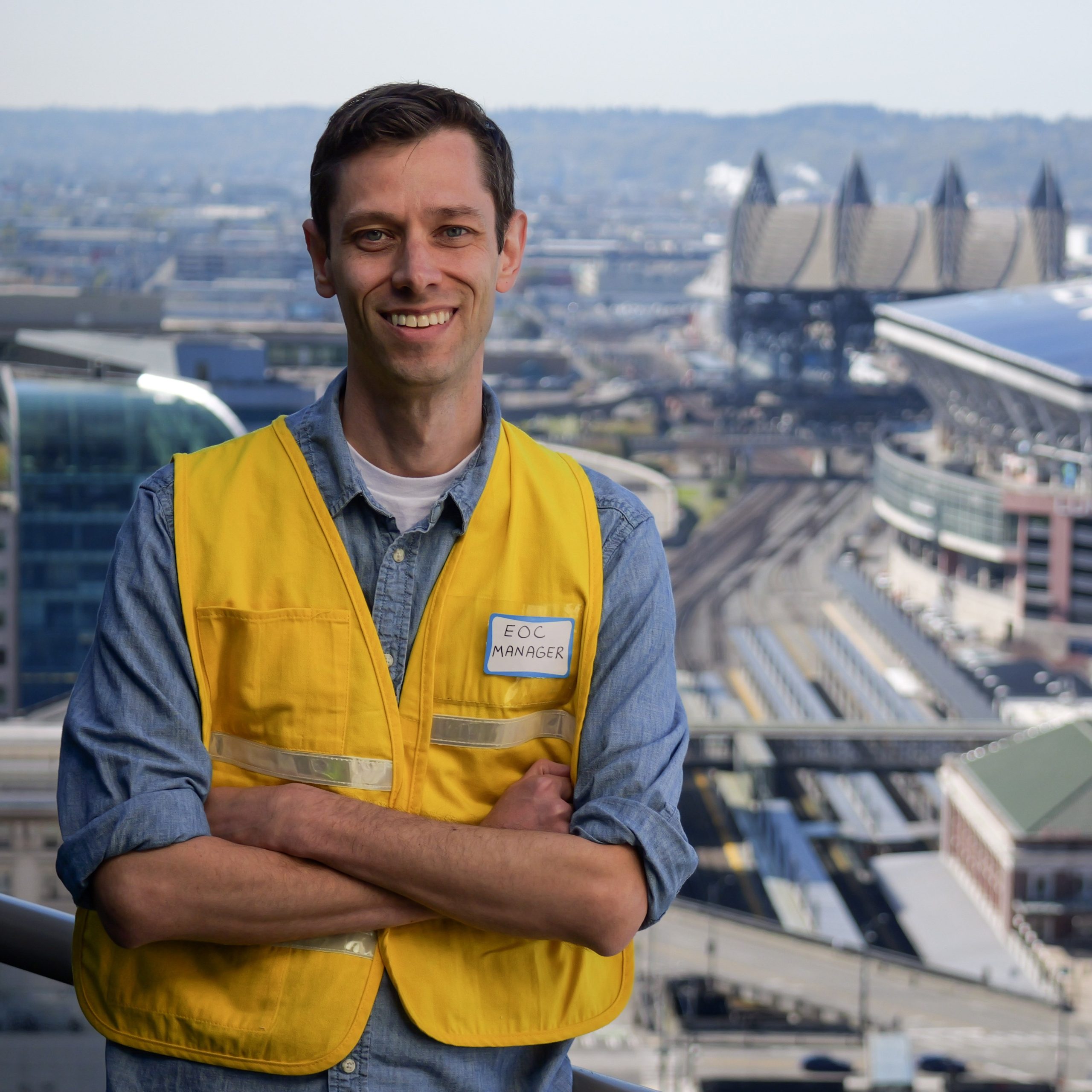 Nick Solari poses for a photo wearing a yellow safety vest with Seattle's downtown stadiums in the background