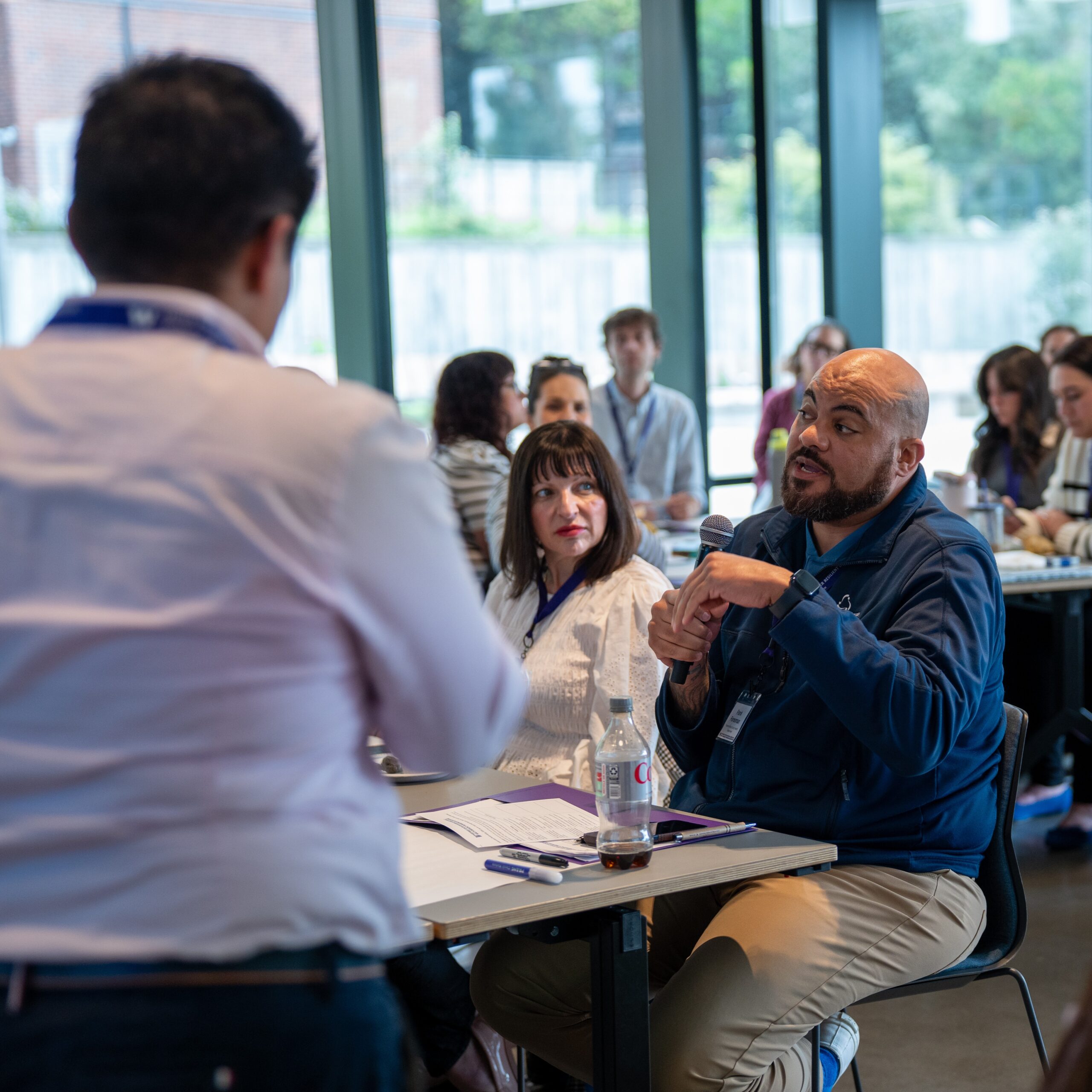 An attendee speaks into a microphone while seated at a table